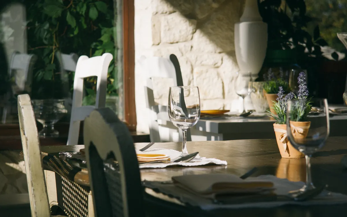 Une table dressée dans la salle ensoleillée d'un bistrot, verres à pied et pots de lavande